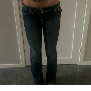 Miss me jeans  - Snygga mörkblå jeans med unika broderade detaljer på bakfickorna. Byxorna har en låg midja och en bootcut-stil som ger en avslappnad look. Perfekta för att lägga till lite edge till din outfit.