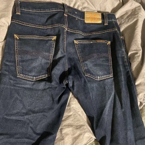 Mörkblå jeans från Nudie Jeans - Säljer ett par mörkblå jeans från Nudie Jeans i storlek 32/32. De är tillverkade av 99% bomull och 1% elastan för en bekväm passform. Inte använda så mycket. Modellen grim tim! Skriv vid funderingar 👍🏻