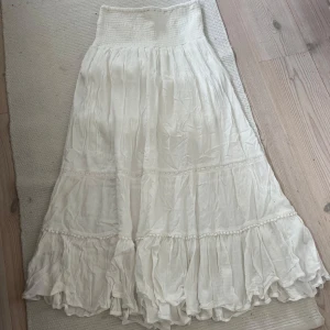 Vit långkjol med volang - Charmig vit långkjol med volangdetaljer och broderade inslag. Kjolen har en luftig och romantisk stil, perfekt för varma dagar. Den elastiska midjan ger en bekväm passform. Original priset var runt 400. Skulle säga att storleken är xxs/xs. Den är bara använd 2/3 gånger.