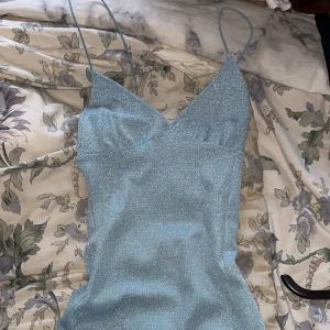 Ljusblå glittrig klänning från H&M - Snygg ljusblå klänning från H&M med glittrigt material och smala axelband. Klänningen har en omlott-design och en öppen rygg💕