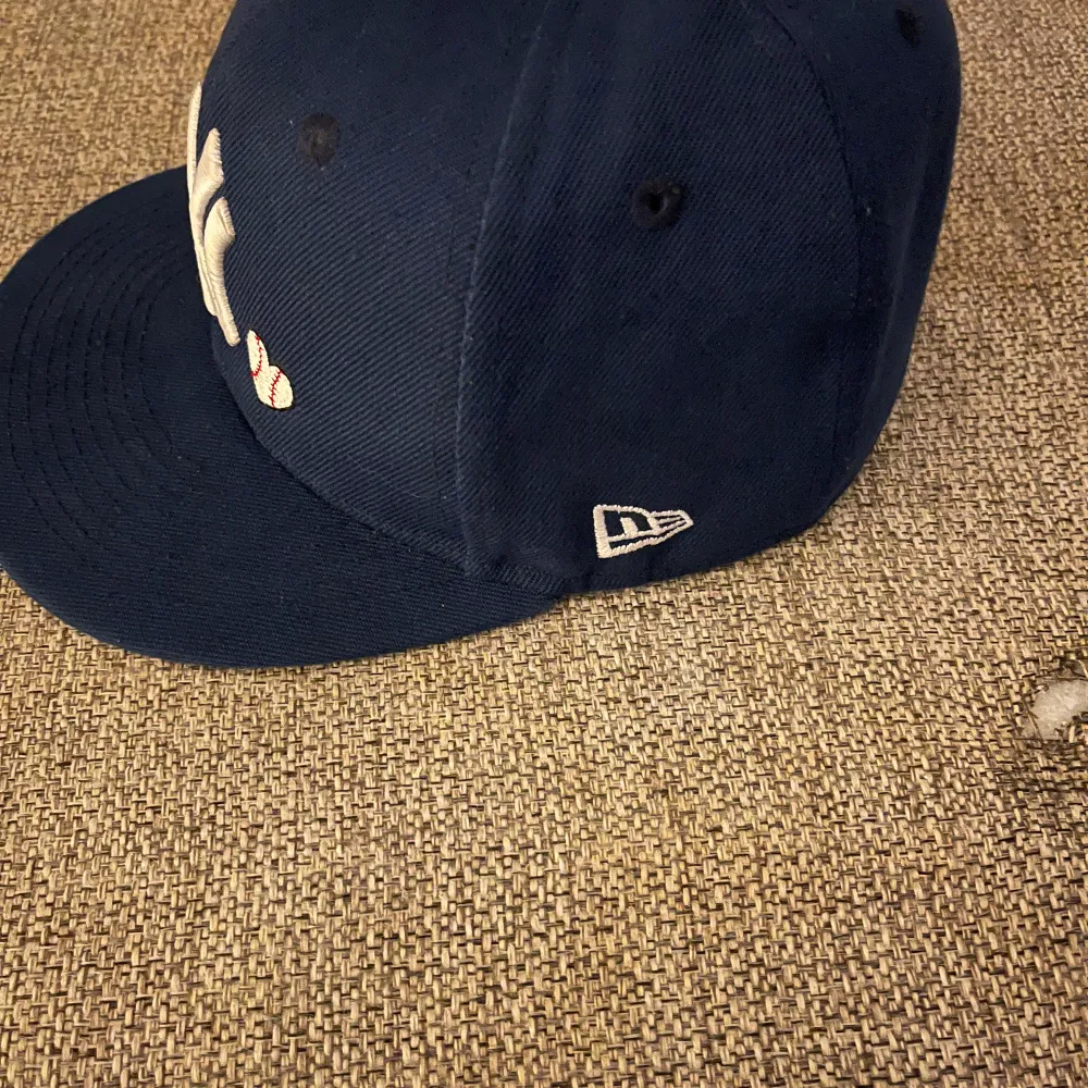 Snygg mörkblå keps från New Era med broderad logga framtill och World Series-märke på sidan. Perfekt för sportiga tillfällen eller som en stilren accessoar.. Asusteet.