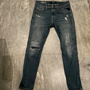 Blå jeans från Replay - Säljer ett par snygga blå jeans från Replay med slitna detaljer och en klassisk femficksdesign. Jeansen har en normal passform och är perfekta för en avslappnad stil. Midjan är 31 och längden 32. Modellen är replay anbass!