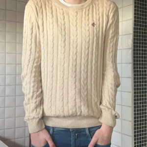 Beige stickad tröja från Morris - Säljer en stilren beige stickad tröja från Morris med kabelstickat mönster. Tröjan har rund hals och långa ärmar, perfekt för kyligare dagar. Skicket är 8/10 och modellen på bilden är cirka 183 lång och väger cirka 65-70kg.