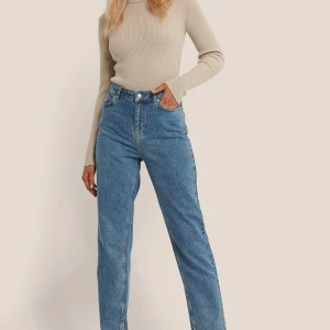 Blå jeans från NA-KD - Säljer ett par klassiska blå jeans från NA-KD i storlek 42. De har en hög midja och en straight passform, perfekt för en avslappnad stil. Jeansen har slits på insidan. Jeansen har en dragkedja och knapp framtill.