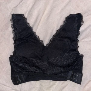 Svart spetsdetaljerad topp - Snygg svart topp med spetsdetaljer och justerbar knäppning. Tillverkad i en mjuk och stretchig blandning av nylon och elastan. 