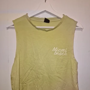 Gul topp från Gina Tricot - Säljer en gul topp från Gina Tricot med texten 'Miami Beach' tryckt i vitt på bröstet. Garderobsrensning så kika gärna på övriga auktioner.