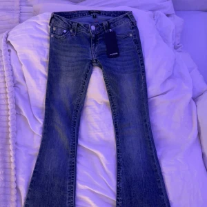 Blå bootcut jeans från True Religion - Helt nya! Snygga low Waist bootcut jeans från True Religion med as nice rosa stygn. Samt märkets ikoniska logga på bakfickan. Perfekta i alla tillfällen och är super lågmidjade. Jag är 170 lång. Säljer för dem inte kommit till användning. Det står att storleken är 25. 