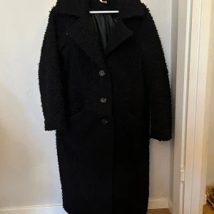 Svart teddykappa XS - En svart teddykappa från indiska storlek XS. Oversized. Är normalt en stor S eller M. Välanvänd jacka.  Har sytt på små hakar (se bild) som knappt syns för att kunna ha kappan knäppt hela vägen upp till halsen vid behov när det är kyligare. 