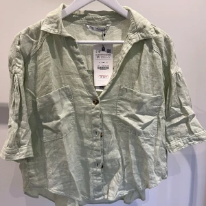 Ljusgrön linneskjorta från Zara - Säljer en superfin ljusgrön skjorta från Zara i storlek M. Skjortan är gjord av linne och har en avslappnad passform med korta ärmar. Den har två stora fickor framtill och knappar hela vägen ner. Perfekt för vår och sommar!