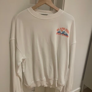 Vit sweatshirt med Vail Alpine Resort-tryck - Säljer en vit sweatshirt med coolt Vail Alpine Resort-tryck i blått och orange. Tröjan har en avslappnad passform och är perfekt för både chill och äventyr. Den är i bra skick och redo för nya äventyr. Perfekt för höst och vår! Storleken är xs men sitter som M
