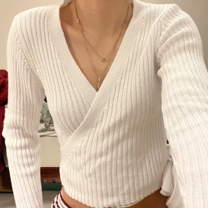 Vit ribbad omlottopp - Säljer en superfin vit ribbad omlottopp med v-ringning. Den har långa ärmar, perfekt för både vardag och fest. Materialet är mjukt och stretchigt, vilket gör den bekväm att bära hela dagen. Passar perfekt till höst och vår outfits! 💫 Använd 1 gång! Passar upp till S