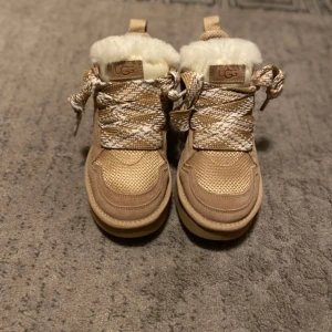 UGG Lowmel 'Sand' - Helt nya och oanvända UGG Lowmel Sand Dessa vinterskor erbjuder både värme och komfort med en vattenavvisande design och halkfri sula. Den stilrena färgen gör dem perfekta för både vardag och mer eleganta tillfällen under vintermånaderna.