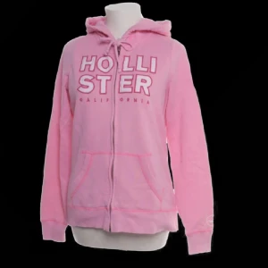 Rosa hoodie från Hollister - Säljer en superfin rosa hoodie från Hollister i storlek M. Den har en dragkedja framtill och en mysig huva. Perfekt för en avslappnad stil eller kyliga dagar. Lite slitage syns på baksidan, men annars i bra skick. Passar perfekt till jeans eller leggings! ❤️