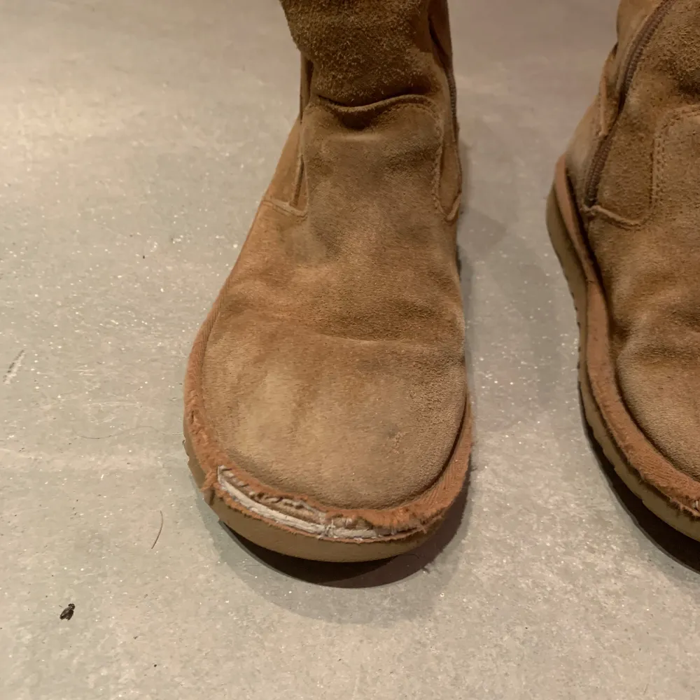 Säljer ett par bruna UGG boots i mocka med mysigt foder inuti. De har en praktisk dragkedja på sidan för enkel på- och avtagning. Perfekta för kalla vinterdagar när du vill hålla fötterna varma och bekväma. Använda men i bra skick.. Skor.