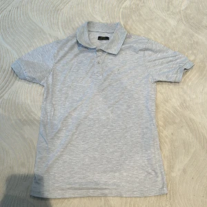 Grå pikétröja från Ralph Lauren - Säljer en stilren grå pikétröja från Ralph Lauren i mycket bra skick. Tröjan har en klassisk krage med tre knappar och det ikoniska broderade logotypen på bröstet. Perfekt för både vardag och lite finare tillfällen. Passar bra till jeans eller chinos!