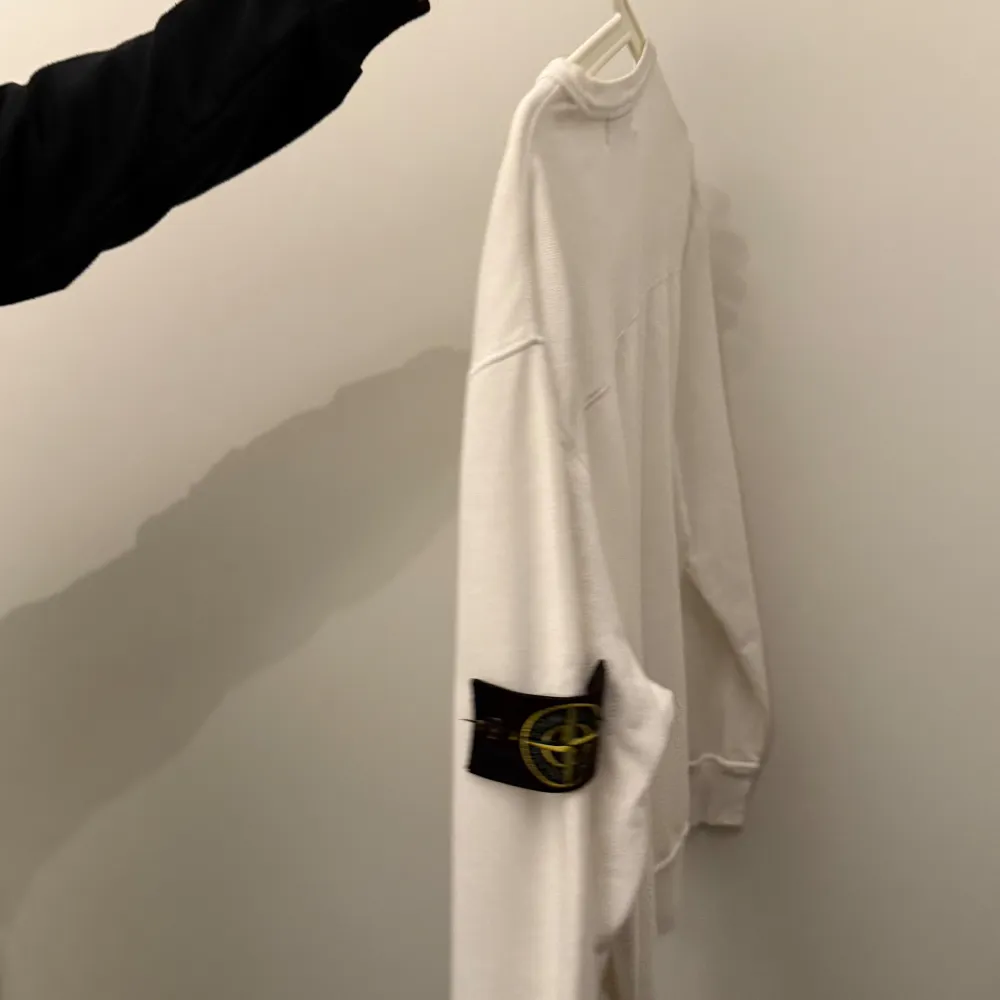 Säljer en stilren vit tröja från Stone Island. Den har en klassisk design med långärmade ärmar och en rund halsringning. Tröjan är i mycket bra skick och har det ikoniska Stone Island-märket på ärmen. Perfekt för både vardag och fest!. Tröjor & Koftor.