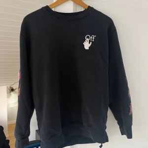 Svart sweatshirt från Off-White - Säljer en svart sweatshirt från Off-White med coola rosa detaljer på ärmarna och ryggen. Tröjan har en avslappnad passform och är perfekt för både höst och vår. Den är i bra skick och redo för nya äventyr. Passar perfekt till jeans eller joggers för en casual look! Passar S-M