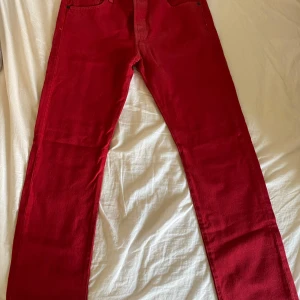 Röda jeans från Levi's - Säljer ett par snygga röda Levi's jeans i storlek W34. De är i bra skick och har en klassisk straight passform. Perfekta för att liva upp garderoben med lite färg! De har knappar framtill och är tillverkade i bomull. Passar både till vardags och fest.