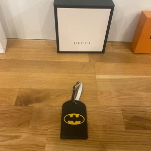 Svart bagagetag med Batman-logga - En Cool svart bagagetag med den ikoniska Batman-loggan i gult. Perfekt för att ge din väska en unik touch och lättare hitta den på bagagebandet. Tillverkad i syntetmaterial med plats för namn och kontaktuppgifter. En stilren och praktisk accessoar för alla Batman-fans!