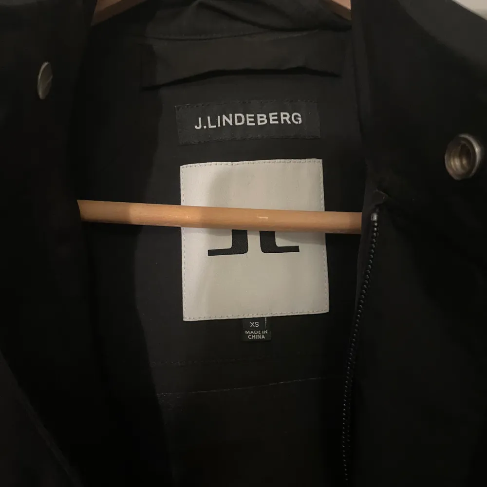 Säljer en stilren svart kappa från J.Lindeberg i mycket bra skick. Den har en minimalistisk design med dragkedja och knappar framtill. Perfekt för höst och vår, och passar både till vardags och fest. Kappan är långärmad och gjord i ett syntetmaterial som ger en elegant look.. Jackor.