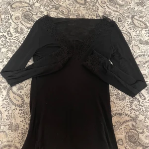 Svart långärmad klänning med spetsdetaljer - Säljer en svart intimissmi tröja med v-ringad spetsdetalj. Iprincip använd 3 gånger, köptes för nån månad sen, OBS en jätte liten fläck som Inge går bort på armen som ni ser på en av bilderna 