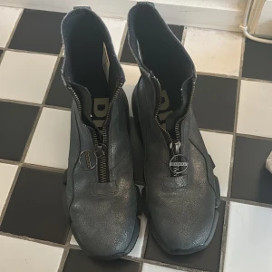 Grå boots från Diesel - Säljer ett par grå boots från Diesel i mycket bra skick. De har en cool dragkedja framtill och en robust sula med Diesel-logga. Perfekta för höst och vinter med sin stilrena design och slitstarka material. Passar både till vardags och festliga tillfällen.