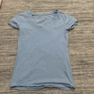 Ljusblå t-shirt från Basic You - Säljer en enkel och stilren ljusblå t-shirt från Basic You i storlek XS. T-shirten har en v-ringad hals och korta ärmar, perfekt för vardagsbruk. Materialet känns mjukt och bekvämt mot huden. Passar bra till både jeans och kjol för en avslappnad look.