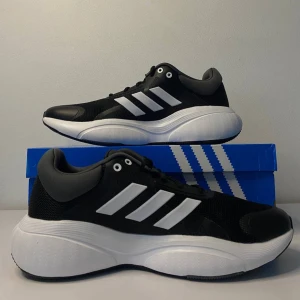 sneakers Adidas - Säljer ett par snygga och bekväma svarta sneakers från Adidas med vita detaljer. Skorna har en modern design med den klassiska tre-randiga looken på sidan. Perfekta för både vardag och träning. De är i nytt skick och kommer i originalkartong.