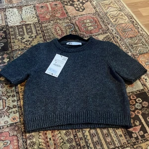 Mörkgrå stickad tröja från Zara - Säljer en superfin mörkgrå stickad tröja från Zara i nytt skick. Den har korta ärmar och en ribbad kant vid ärmslut och nederkant. Perfekt för höst och vinter, och den är både mysig och stilren. Passar perfekt till allt och jag har bara haft på mig den en gång!