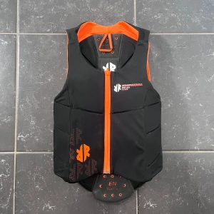 Ryggskydd från Komperdell - Säljer ett svart ryggskydd med orange detaljer från Komperdell. Smidig och skön. Den är i mycket bra skick! 