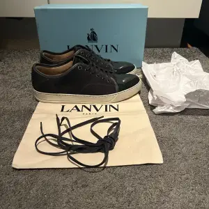 Säljer ett par snygga mörkgråa sneakers från Lanvin i nyskick Nypris 5000, Uk 10 passar 44-45. Skorna har en stilren design med svarta snören och en glansig captoe. Perfekta nu inför vintern med mörk grå färg passar perfekt till både vardag och fest! Kommer med box dustbag och extra skosnören.