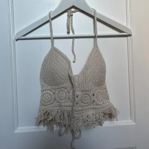 Beige virkad topp - Superfin beige virkad topp med fransar och knytband i ryggen. Perfekt för sommardagar eller festivaler. Den har en bohemisk stil med detaljerade mönster och ärmlös design. Passar perfekt till jeansshorts eller en lång kjol. Köpt i Grekland.