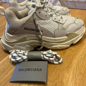 Balenciaga sneakers i vitt, TripleS - Säljer ett par snygga Balenciaga sneakers i vitt. De har en chunky sula och är i mycket bra skick. Skorna har snörning och kommer med extra skosnören. Perfekta för en trendig look!