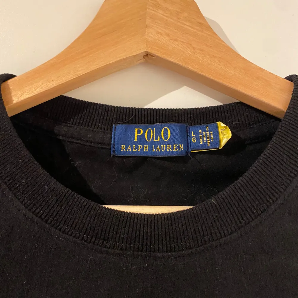 Säljer en klassisk svart t-shirt från Ralph Lauren med det ikoniska röda logotypbroderiet på bröstet. T-shirten är i bomull och har en normal passform med korta ärmar. Perfekt för både vardag och fest! 🖤. T-shirts.