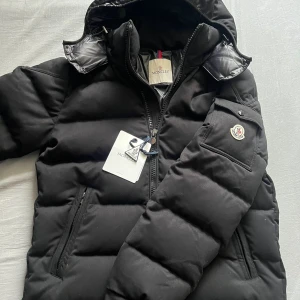  Moncler montegenevre  - INTRSSEKOLL‼️Säljer en snygg svart pufferjacka från Moncler i mycket bra skick. Jackan har en dragkedja framtill och en praktisk huva. Perfekt för kalla vinterdagar och håller dig varm och stilren. Moncler-loggan syns på ärmen. Passar både till vardags och fest!🤩🤩