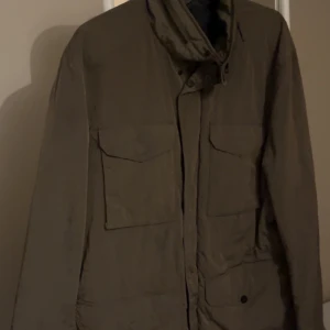 Olivgrön jacka från J.Lindeberg - Säljer en olivgrön jacka från J.Lindeberg i storlek M. Jackan har en stilren design med långa ärmar och praktiska fickor framtill. Perfekt för höst och vår, med en bekväm passform och snygga detaljer. Passar både till vardags och lite finare tillfällen. 