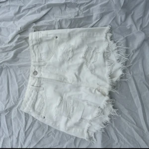 Vita jeansshorts från Shein - Säljer ett par vita jeansshorts från Shein i storlek XS. De har en snygg distressed look med slitna detaljer och fransiga kanter. Dem är ganska stora i storleken så dom passar nog bäst om man har S.💕