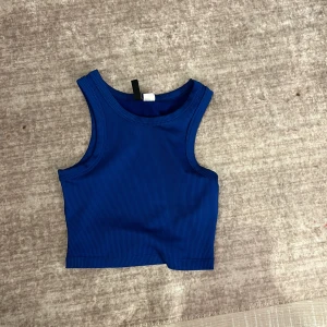 Blå ribbad linnetopp från H&M Divided - Säljer en snygg blå ribbad linnetopp från H&M Divided. Perfekt för sommardagar eller som ett lager under en jacka. Toppen är ärmlös och har en tight passform som framhäver figuren. Använd ett fåtal gånger, så den är i mycket bra skick. Passar perfekt till både jeans och kjol! Säljer för jag inte andvänder den