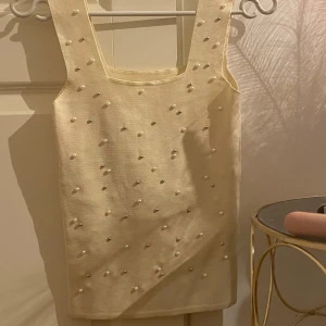 Beige ärmlös topp med pärlor - Säljer en superfin beige ärmlös topp dekorerad med pärlor. Perfekt för en elegant look, kanske till en fest eller speciellt tillfälle. Toppen har en fyrkantig halsringning.
