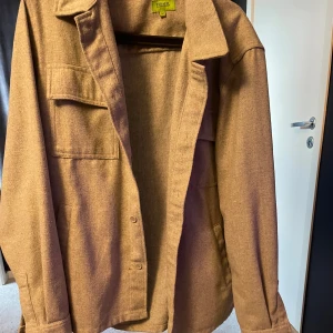 Grå overshirt  - Säljer en snygg grått overshirt  i ullmaterial. Perfekt för höst och vår med sin stilrena design och praktiska fickor. Den har långa ärmar och knappar framtill. Passar både till vardags och lite mer uppklädda tillfällen. Storleken är herr L.