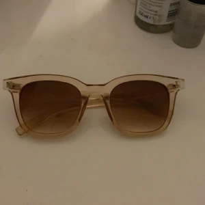 Transparenta solglasögon från Glitter - Snygga solglasögon från Glitter med transparent båge och bruna tonade glas. Perfekta för en solig dag och ger en stilren look. De har en klassisk form som passar de flesta ansikten. Använd dem för att skydda ögonen och se cool ut samtidigt!