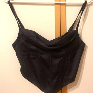 Svart fest satin topp - Festtopp i satin liknande material. Aldrig använd. Kan öppnas och stängas i ryggen med dragkedja. 