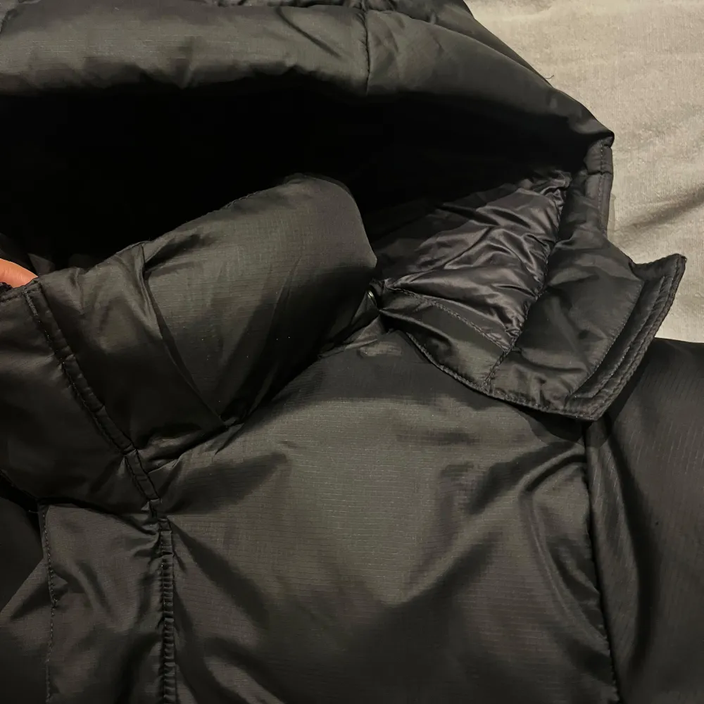 Säljer en svart dunjacka från Helly Hansen i storlek 164. Jackan är perfekt för kalla vinterdagar med sin tjocka vaddering och huva. Den har en stilren design med Helly Hansen-logga på bröstet och ryggen. Jackan är i mycket bra skick och redo för nya äventyr! 🖤Luvan är avtagbar. . Takit.