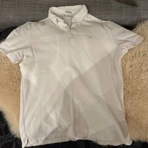 Vit kortärmad skjorta från J.Lindeberg - Säljer en stilren vit kortärmad piké från J.Lindeberg i slim fit. Piké har en klassisk krage med knappar och är perfekt för både vardag och fest. Materialet känns mjukt och bekvämt. Passar utmärkt till sommaren eller som en del av en lager-på-lager-look. Funkar även bra och golfa i. 