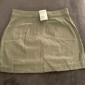 Olivgrön kjol från H&M - Säljer en snygg olivgrön kjol från H&M i storlek 38. Kjolen har en dragkedja baktill och är i ett stilrent och enkelt snitt. Perfekt för både vardag och fest! 🫶