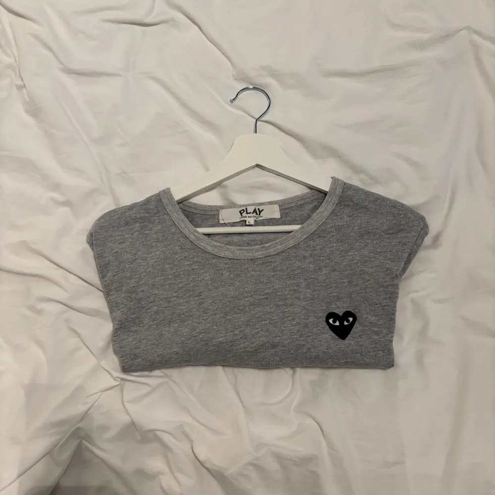 Säljer en stilren grå t-shirt från Comme des Garçons med det ikoniska svarta hjärtat på bröstet. T-shirten sitter som S, skriv vid några funderingar!. T-paidat.