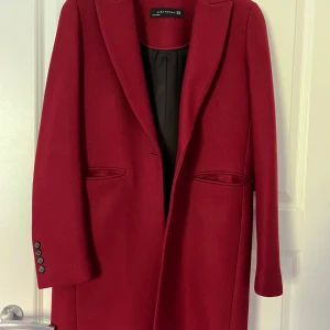 Röd kappa från Zara Woman - Säljer en elegant röd kappa från Zara Woman i storlek XS. Den har en klassisk design med långa ärmar och knappar vid ärmsluten. Perfekt för höst och vinter. Använd några fåtal gånger och har inga defekter. Ull blandning. 