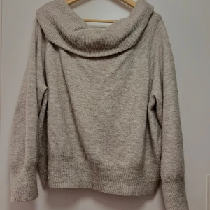 Beige stickad off shoulder tröja - Mysig beige stickad tröja med en bred krage som ger en avslappnad look. Perfekt för kyliga höst- och vinterdagar. Tröjan har långa ärmar och ribbade muddar vid ärmslut och nederkant för extra komfort. Passar både till vardags och mysiga hemmakvällar. Pris kan diskuteras!!💘