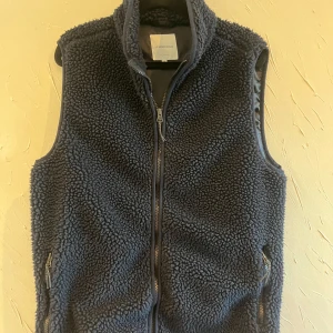 Mörkblå fleeceväst från Lindbergh - Säljer en mörkblå fleeceväst från Lindbergh i storlek S. Västen har en dragkedja framtill och två praktiska fickor med dragkedjor. Perfekt för kyliga dagar när du vill hålla dig varm och bekväm. Passar bra till både vardag och fritid.