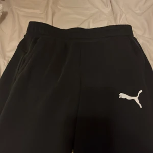 Svarta mjukisbyxor från Puma - Säljer ett par svarta mjukisbyxor från Puma i storlek S. De är superbekväma och perfekta för en chill dag hemma eller en snabb tur till gymmet. Byxorna har en elastisk midja och det klassiska Puma-loggan i vitt på benet. 